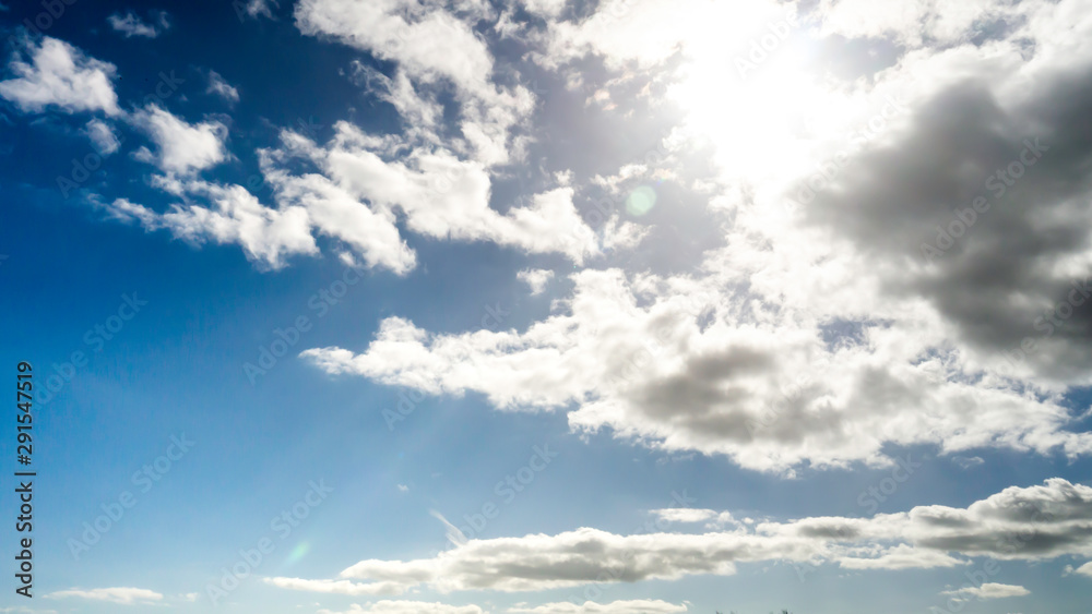 Obraz premium Sun breaking through white clouds with vibrant blue sky background taken on a warm spring/summer day.