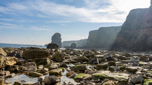 Rocks and rock pools taken at Marsden Beach in South Shields, Tyne and Wear, England UK. Scenic view with coastline, cliffs, eroded rock, sunny blue sky and clouds. photo