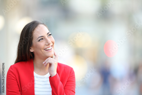 Happy woman in red thinking looking at side outdoors