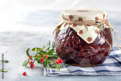 Lingonberry jam in a glass jar with  cranberries, cowberries on light background