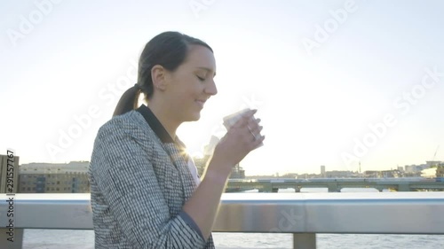 Steady cam view of an attractive caucasian business woman commuter drinking coffee walking leaving the office on London bridge at sunset