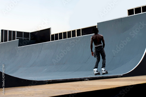 Back view of Afro American inline roller skater rolling off the ramp