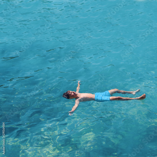 Cute European boy in blue swim pants floating in transparent blue sea water. He is enjoying his summer holidays in Spain.