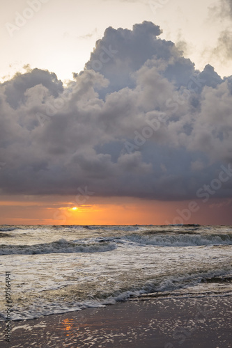 Setting sun between the horizon and a large storm cloud over sea