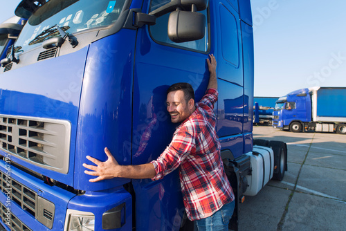 Truck driver loves his job. Professional trucker driver hugging his truck cabin loving his job.