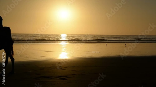 A berber riding a camel across golden sand bridge made by the setting sun in the surface of a wet sand beach in Agadir, Morocco.
