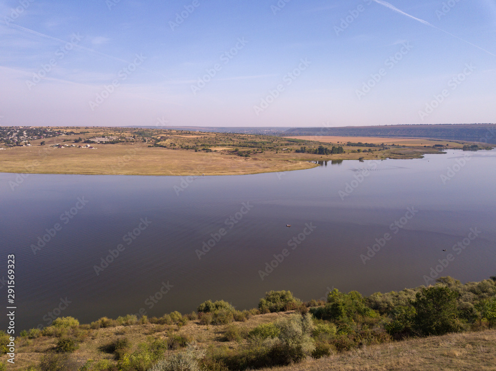 Top view of Dnestr (Dniester) river in autumn. River surrounds yellow field and green forest. Moldova republic of.