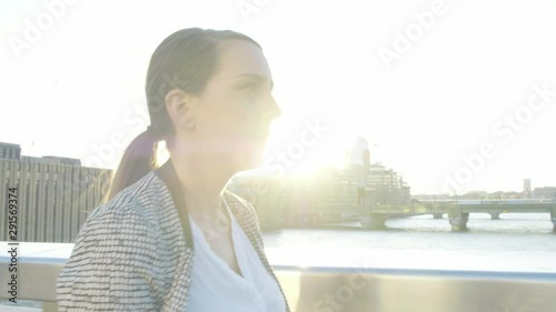 Steady cam view of an attractive caucasian business woman commuter walking on London bridge at sunset