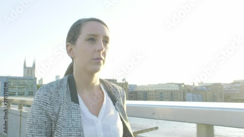 Steady cam view of an attractive caucasian business woman commuter walking on London bridge at sunset