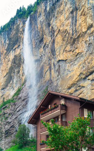 Lauterbrunnen, Bern / Switzerland - July 3rd, 2019: The Staubbach Fall with a traditional alpine house in the foreground