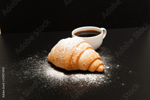 Croissant with a cup of coffee on a black background