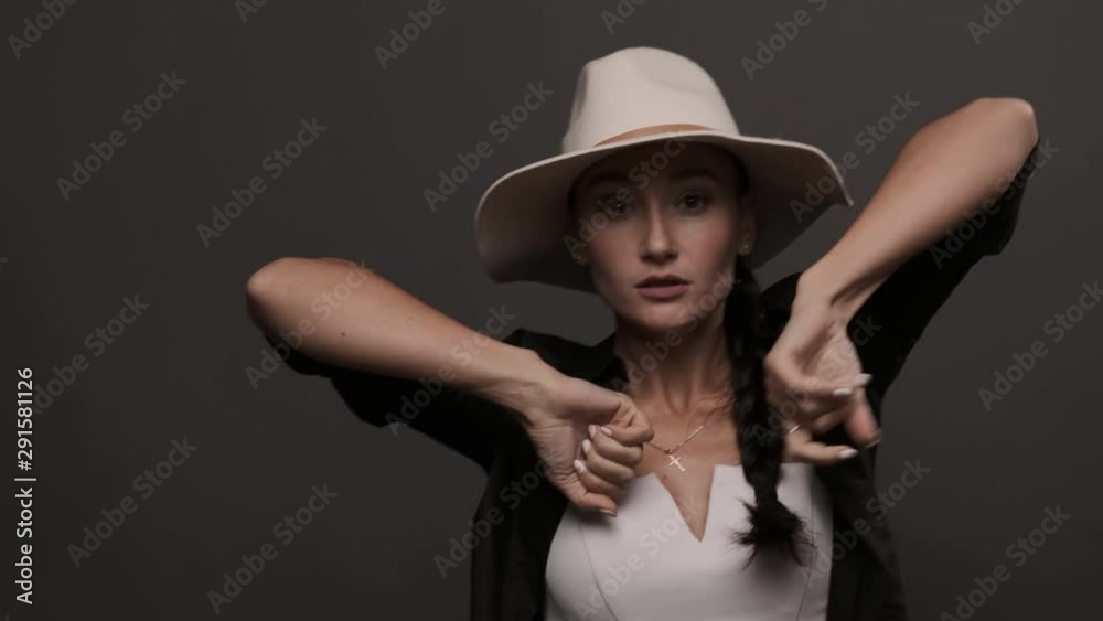Stylish girl in hat performing cool dance and looking at camera. Caucasian woman dancing in studio. Contemporary dance movement. Listening to music. Female dancer enjoying modern waacking dance style Stylish girl in hat performing cool dance and looking at camera. Caucasian woman dancing in studio. Contemporary dance movement. Listening to music. Female dancer enjoying modern waacking dance style