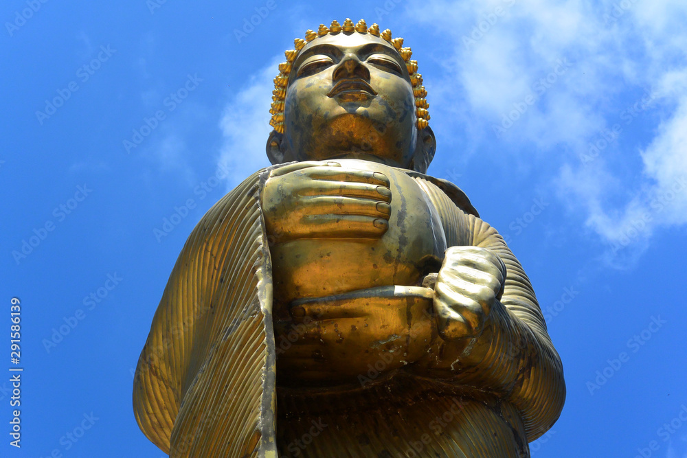 Obraz premium Golden statue of a standing Buddha against a blue sky