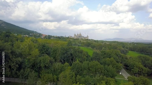golf course in a forest of ash with the historic monastery of escorial crowning a hill, aerial view over hills photo