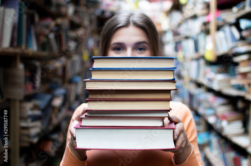 Fotografie girl student holds a stack of books in the library, she searches for literature