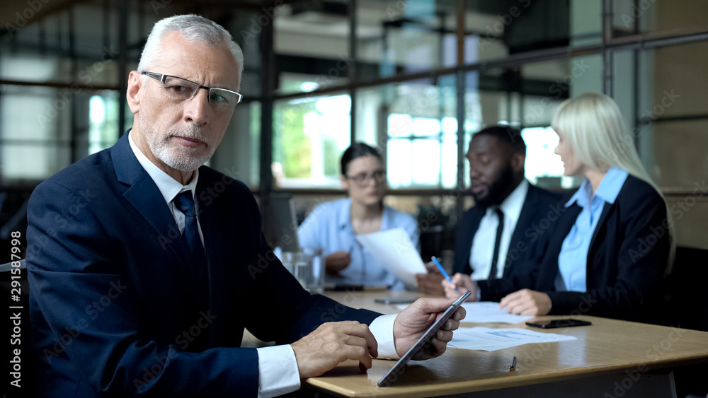 Concerned company boss making decision tablet in hands, managers discussing plan Concerned company boss making decision tablet in hands, managers discussing plan