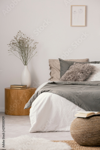 Wooden nightstand table next to king size bed with white and grey bedding in simple bedroom interior photo