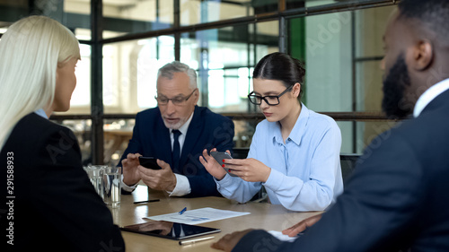 Businesspeople looking indifferent partners using smartphones, gadget addiction