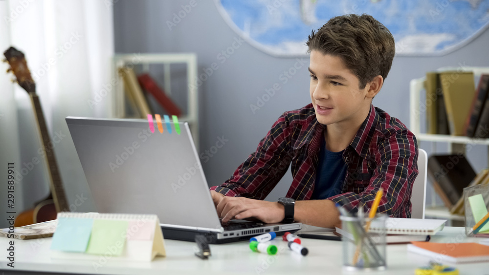 Schoolboy playing online game on laptop at home sitting table, teenage free time Schoolboy playing online game on laptop at home sitting table, teenage free time