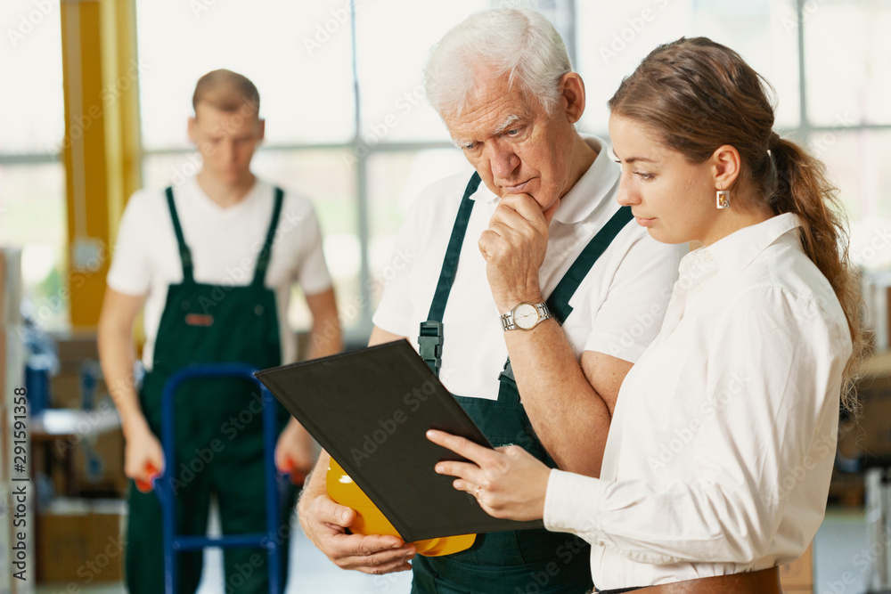 Senior plant manager in emerald green uniform and office worker checking documents together Senior plant manager in emerald green uniform and office worker checking documents together
