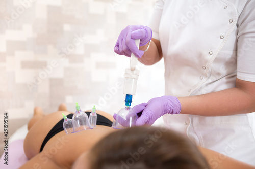 A young female doctor performs vacuum cup therapy on a young brunette woman in a body care salon.