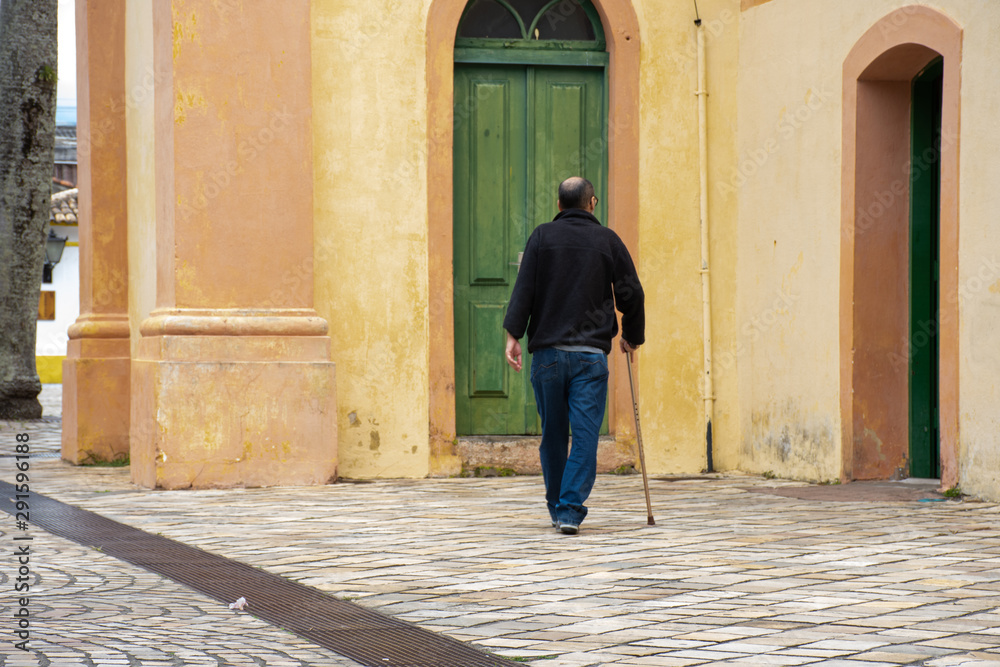 Disabled man walks with walking stick and difficulty on the street Disabled man walks with walking stick and difficulty on the street