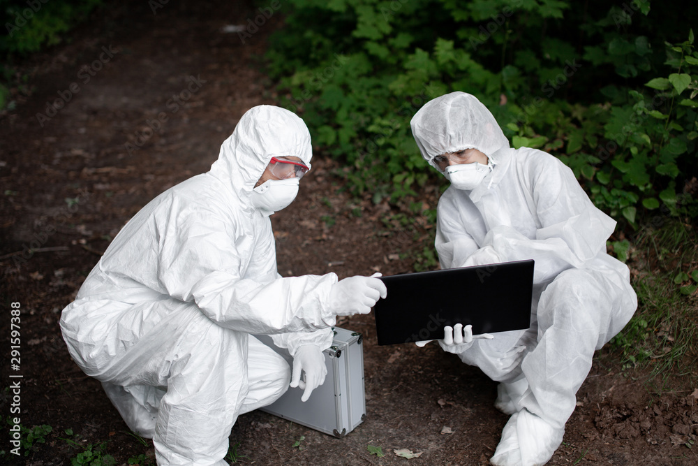 Ecological problem. Pollution. Examine soil. Scientist working in forest in protective mask and suit taking water and soil samples. Chemist makes an analysis of the environment for radiation. Ecological problem. Pollution. Examine soil. Scientist working in forest in protective mask and suit taking water and soil samples. Chemist makes an analysis of the environment for radiation.