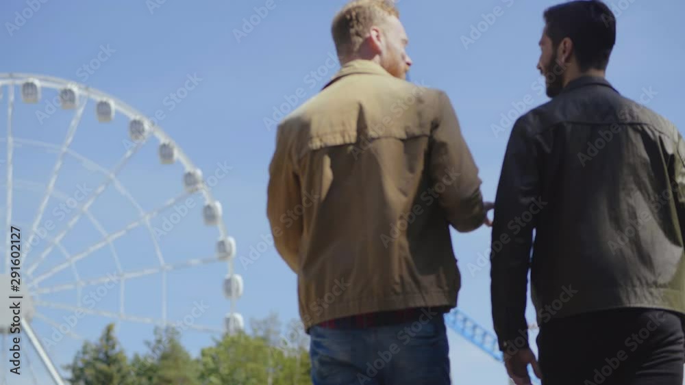 Back side view of two male friends that walk in amusement park and discuss something