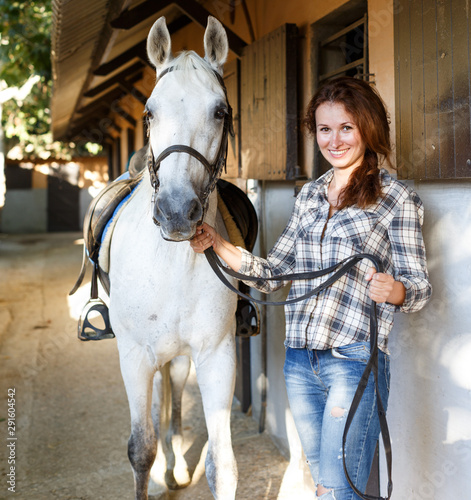 Female farmer standing with white horse at stable outdoor