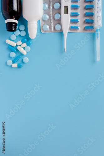 Treatment of colds and flu. Various medicines, a thermometer, sprays from a stuffy nose and a pain in a throat on a blue background. Copy space. Medicine flat lay