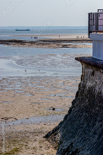 people walking far in the sea when tide is low, ship on background, guardrails on foreground