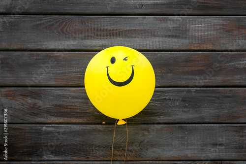 Happiness emotion. Yellow balloon with smile on dark wooden background top view copy space