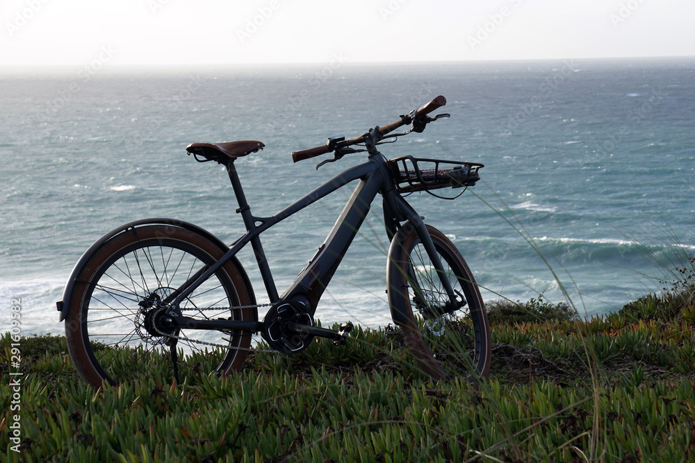 classic style electro powered bicycle with front rack at the coast with ocean in the background