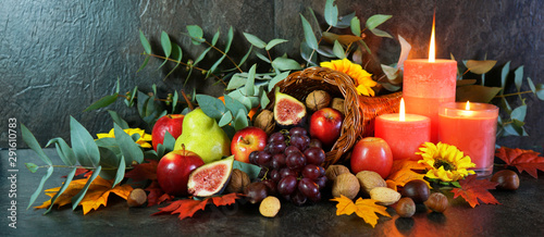 Happy Thanksgiving cornucopia table setting centerpiece decorated with autumn leaves, fruit, nuts and orange burning candles, web banner. photo