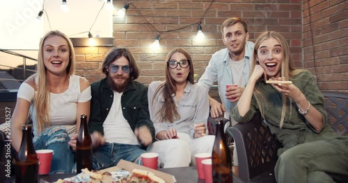 Happy friends watching sports game on tv, cheering for favorite team and making win gesture