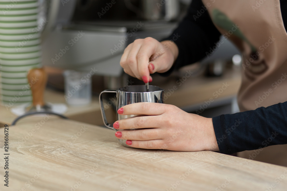 An apron barista pours hot cocoa into a cup. Barista work in a coffee shop