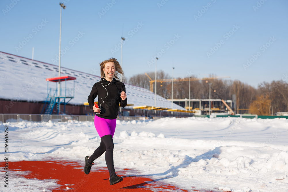 girl in sportswear run on the red track for running on a snow-covered stadium Fit and sport lifestyle. Run and listening music. Sport lifestyle