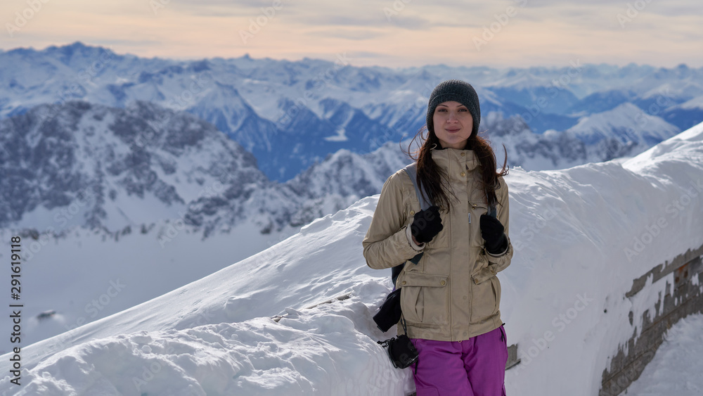 Female traveler on the top of Zugspitze at sunset. It is the highest peak of Wetterstein mountains in Germany.  It lies south of the town of Garmisch-Partenkirchen. Alps.