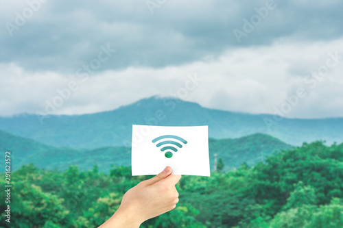 Business Communication Concept : Hand holding paper with cutout wireless signal in green natural background.