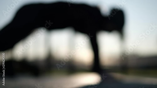 Blurred woman silhouette doing a push up at the playground on cold weather breathing deeply. Close up view.
