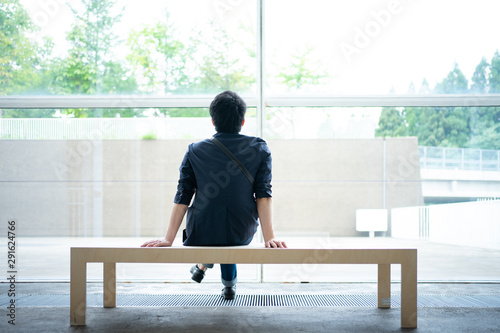 大きな窓の前に設置されたベンチに座る男性