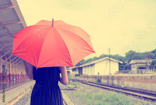 Woman in black dress holding red umbrella walking on railway in a rain day