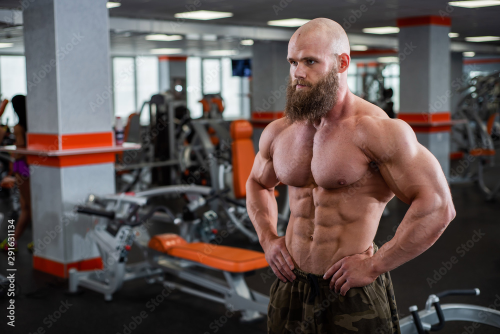 Shirtless male bodybuilder posing in the gym. Relief athlete on a diet before the competition. Muscular chest Men. Great physical shape Shirtless male bodybuilder posing in the gym. Relief athlete on a diet before the competition. Muscular chest Men. Great physical shape