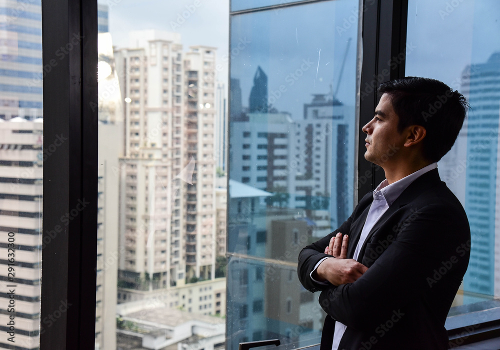 Fototapeta premium A handsome businessman look out of his office window on the tall building and think about the company development and new project in the future/Vision/Business going forward