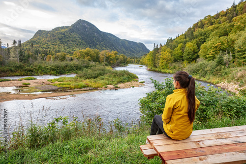 Camping nature woman sitting at picnic table enjoying view of wilderness river in Quebec and autumn foliage forest, Canada travel. Parc de la Jacques-Cartier, Quebec. photo