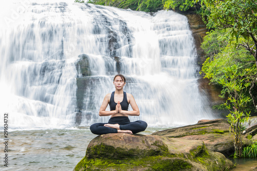 Young asain women practicing yoga at front of grand waterfall.