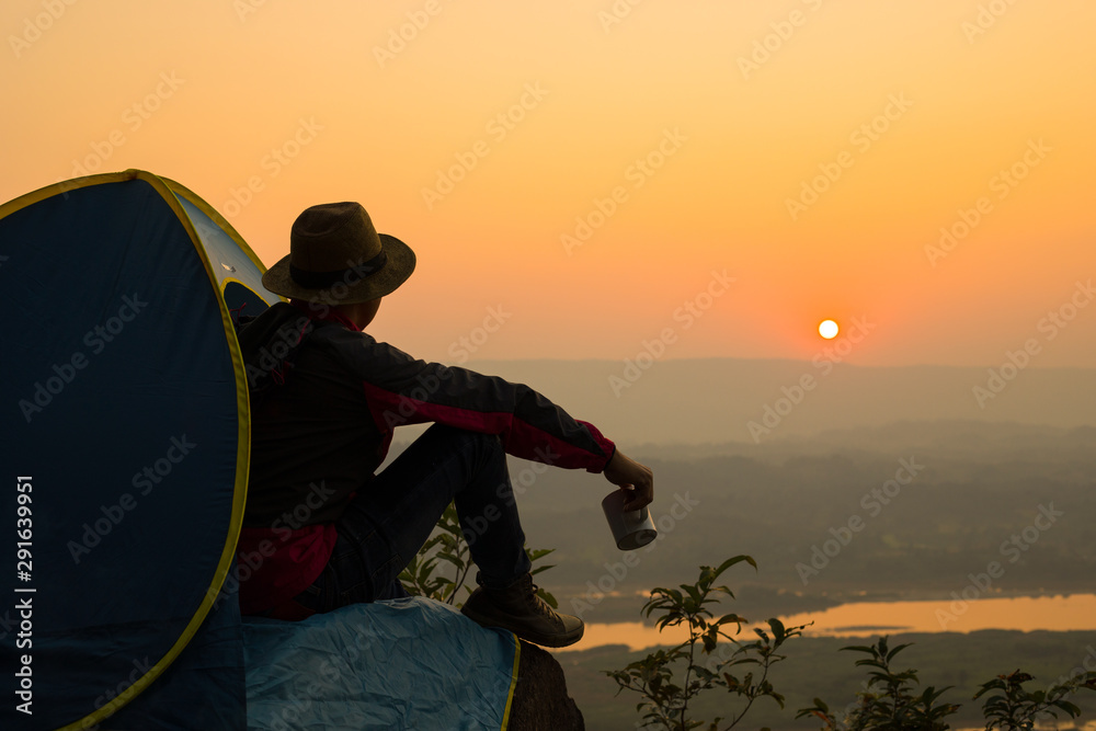 Young man traveler sitting outside the tent on the top of the hill and drinking coffee with beautiful sunrise,Tourist,Tent,Coffee, Sunrise,Sunset