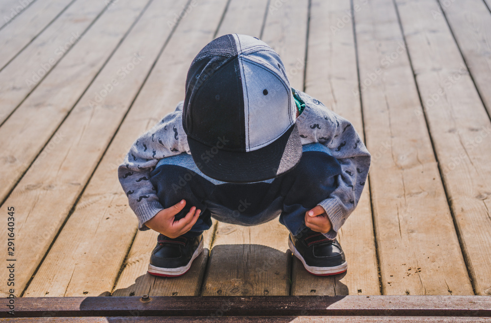 Small boy sitting in squatting position on wooden surface Small boy sitting in squatting position on wooden surface