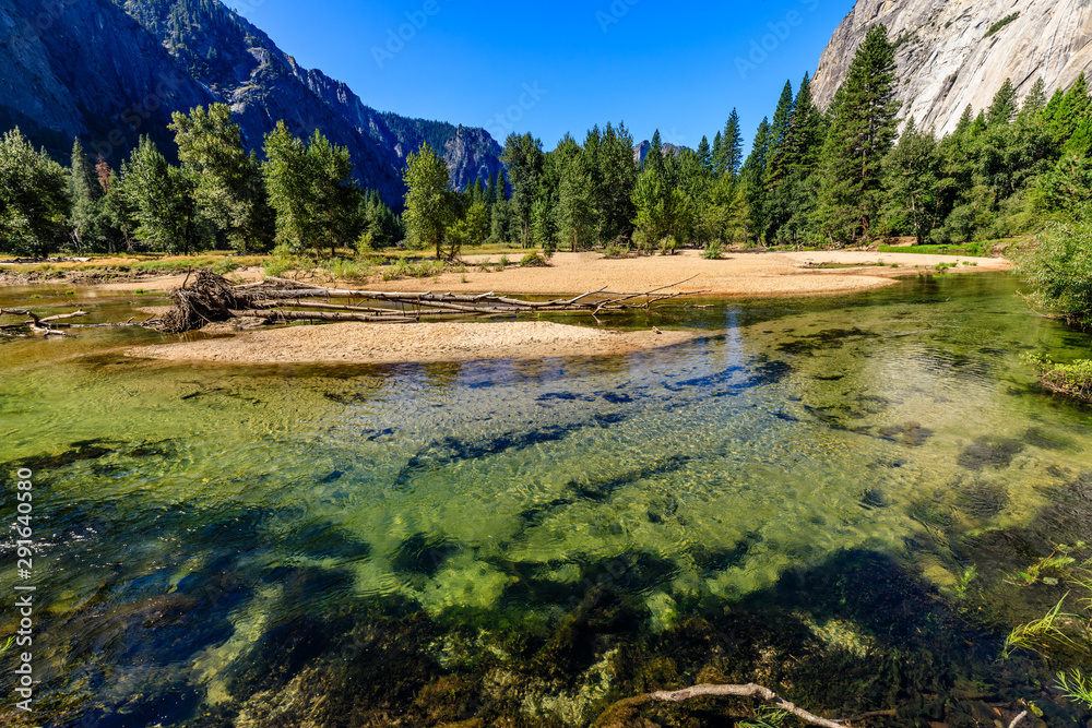 Mossy and sandy bottom of Merced river sparkles green looking towards half dome in Yosemite National Park