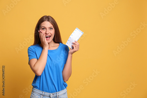 Fotografia Portrait of excited young woman with lottery ticket on yellow background, space